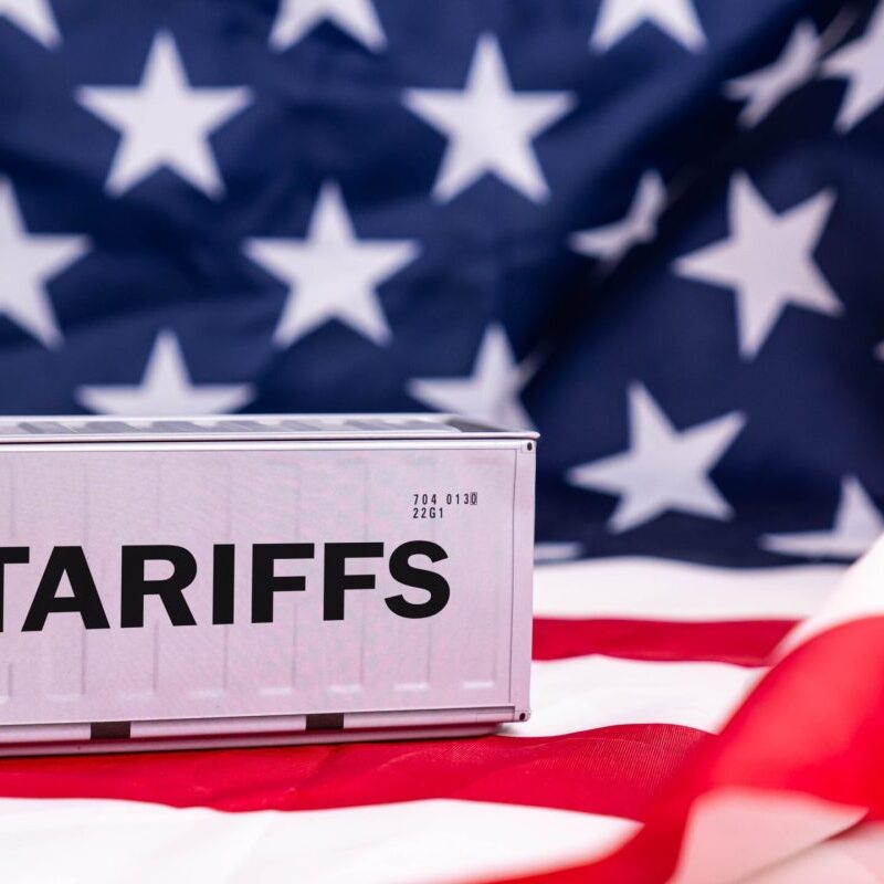 a miniature cargo container with TARIFFS written on the side, sitting on an American flag